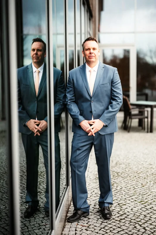 Thomas Kresse stehend im blauen Anzug vor einer Glasfassade mit Spiegelung in Neuruppin