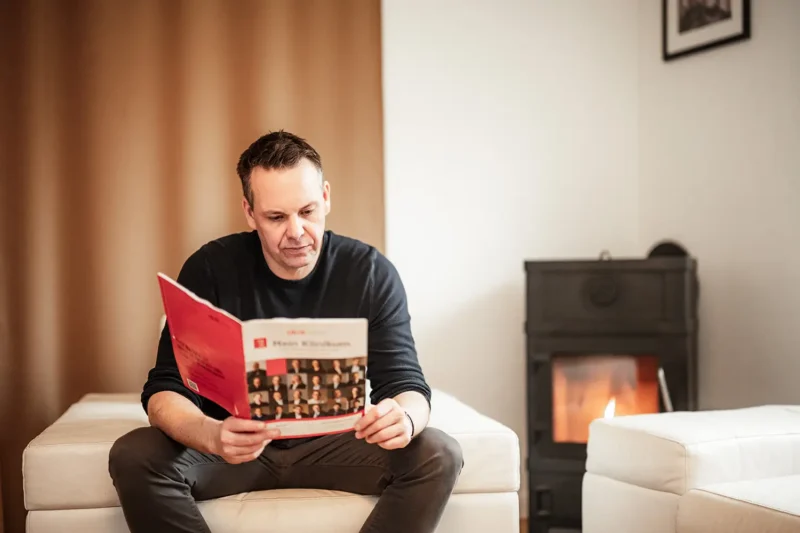 Thomas Kresse liest konzentriert eine Broschüre in einem hellen Raum mit Kamin im Hintergrund – Fokus auf Expertise und Information.