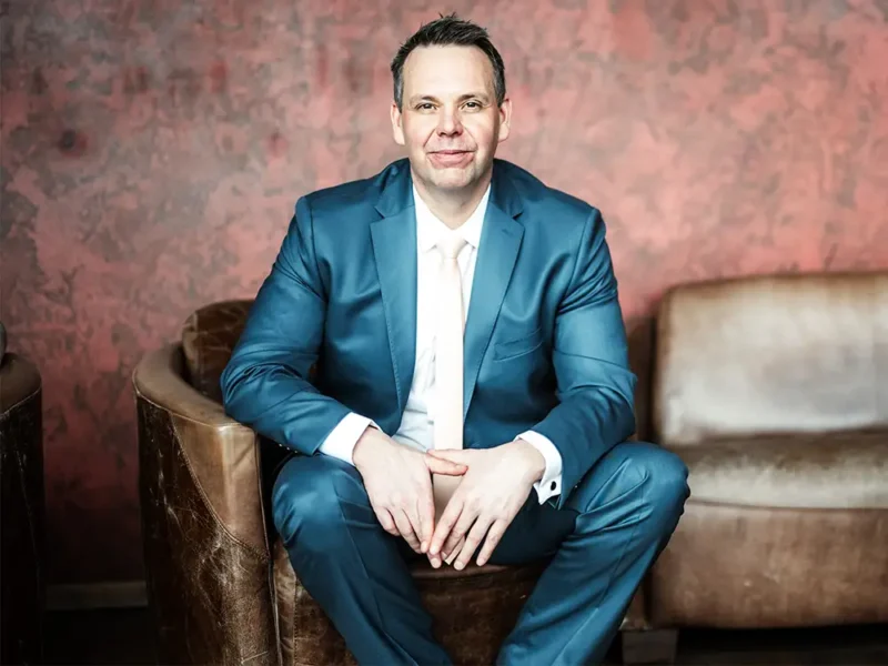 Thomas Kresse sitzt lächelnd in einem Ledersessel vor einer rustikalen Wand